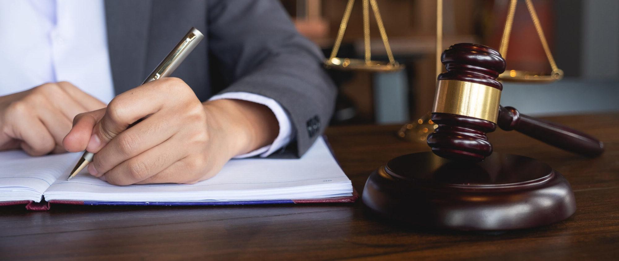 A person taking notes sitting at a table with a judge hammer beside the notebook.