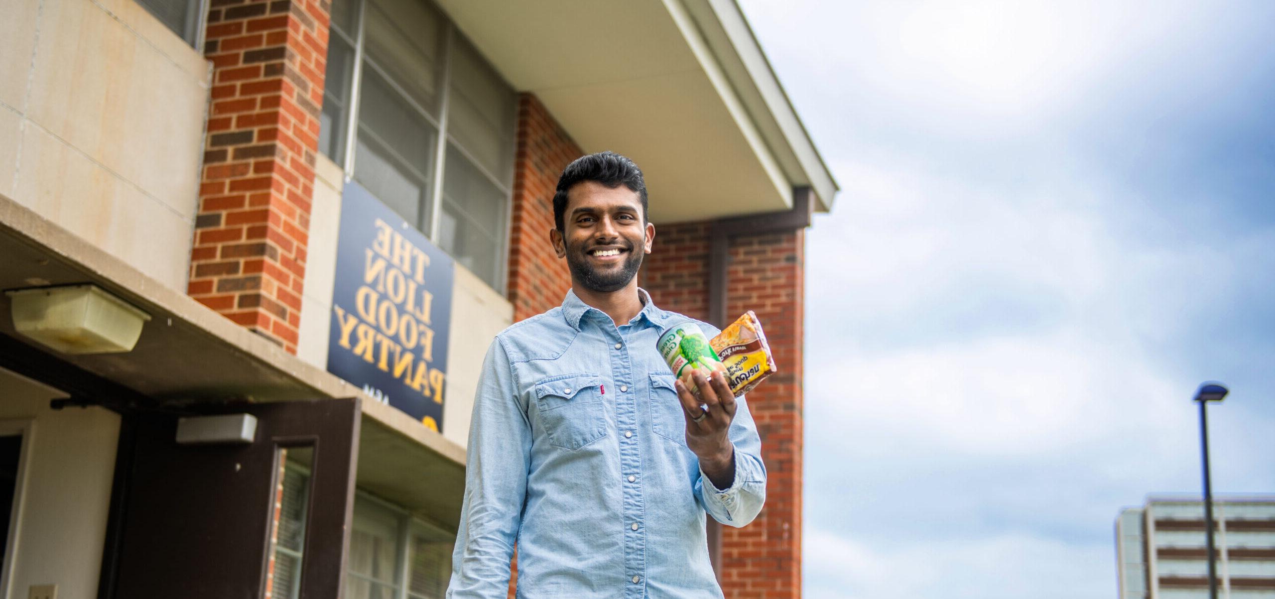 Male student holding on to food in front of the Lion Food Pantry.