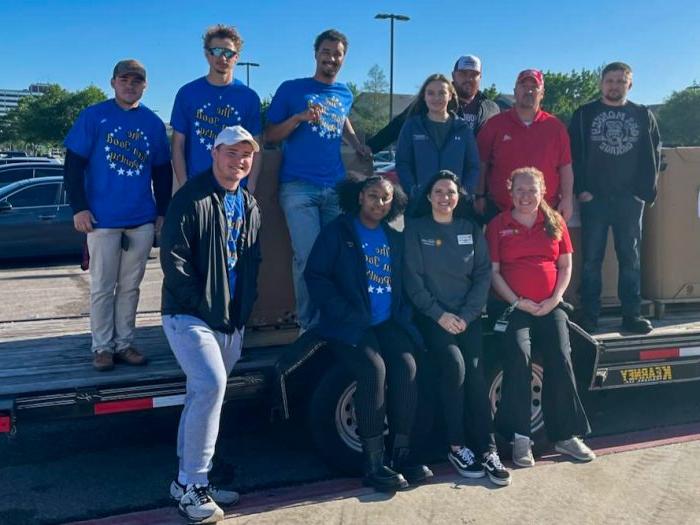 A group of volunteers stand on and around a trailer loaded with boxes from a food drive.