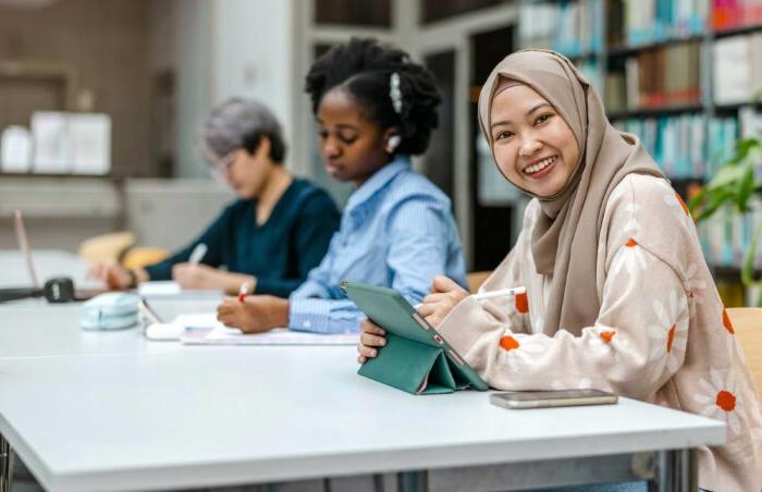 Woman in hijab sitting in the library studying with other students.